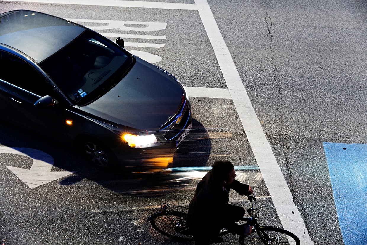 Cyklist og bil ved siden af hinanden i lyskryds